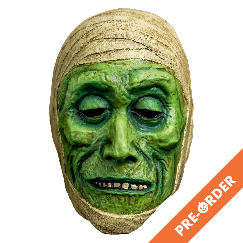 white background, orange diagonal banner at bottom right, white text reads pre-order.  mask, front view. green distressed flesh, eyes slightly closed, mouth with thin lips open showing row of teeth. wrapped in off-white bandages around top of head and perimeter of face.