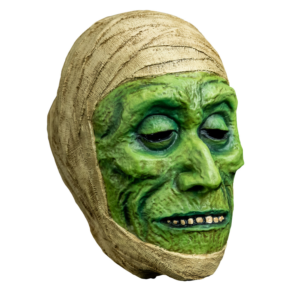 mask, right view. green distressed flesh, eyes slightly closed, mouth with thin lips open showing row of teeth. wrapped in off-white bandages around top of head and perimeter of face.