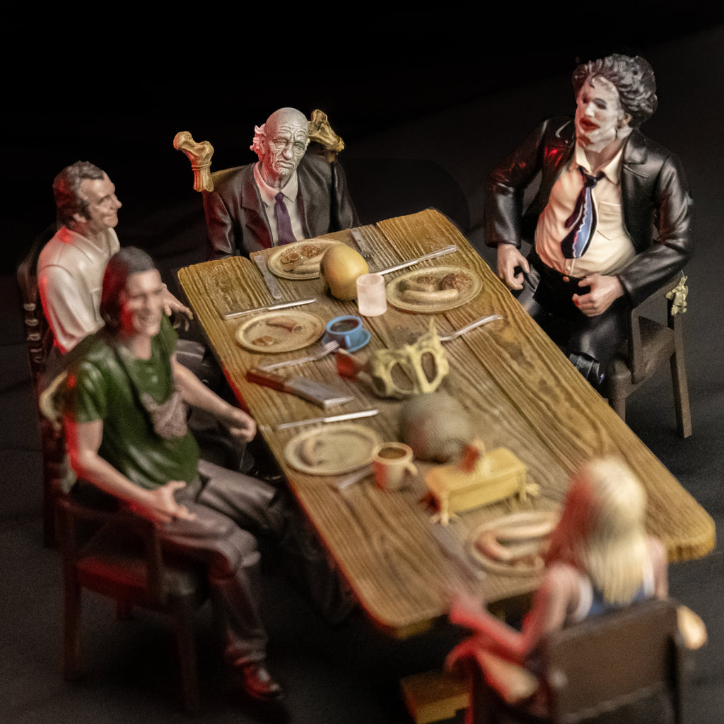 5 Texas chainsaw massacre action figures sitting around dinner table set with plates, cups, silverware, cleaver and bones