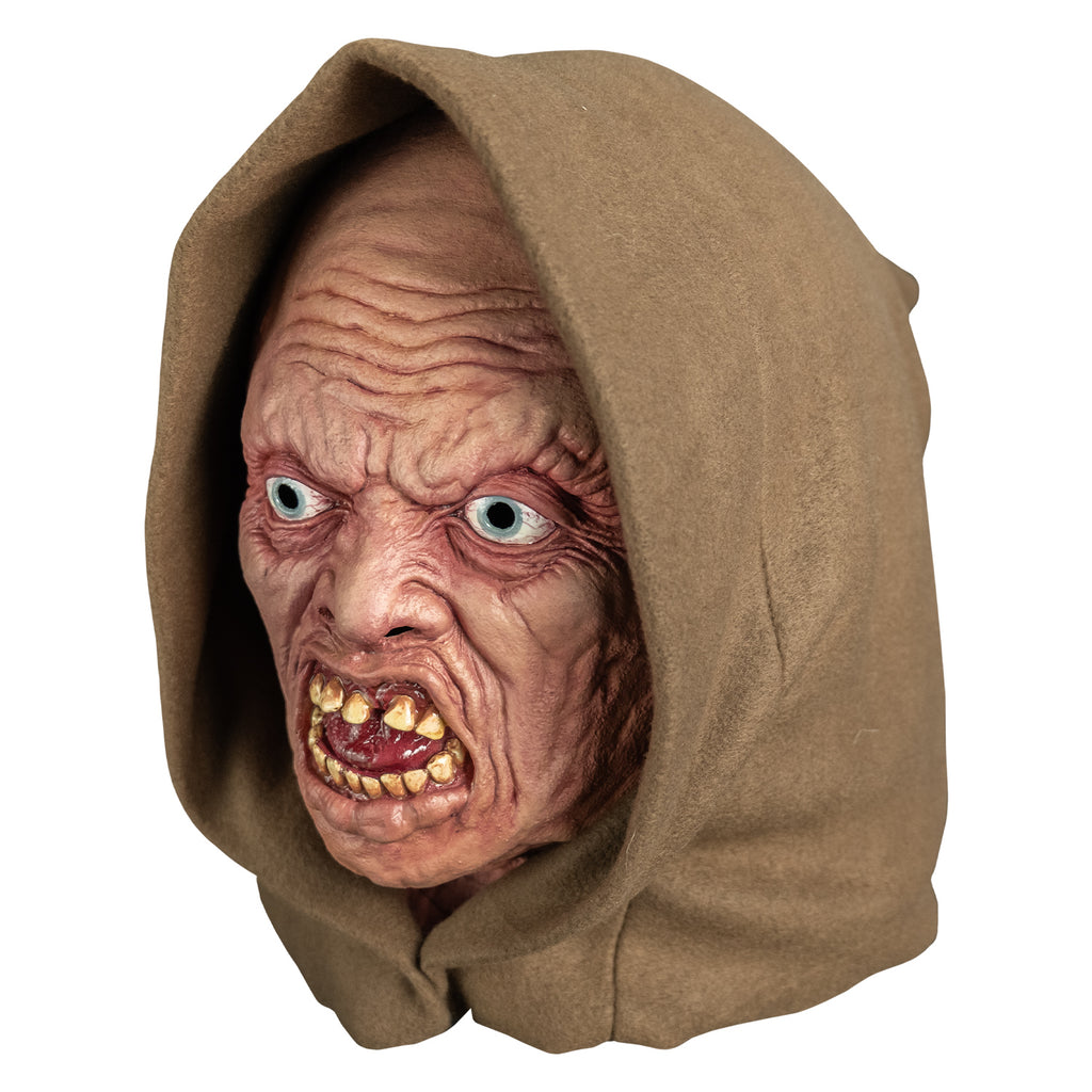 mask, left view. wearing tan hood. pink highly wrinkled flesh. no eyebrows, pale blue irises, mouth open in a snarl showing crooked yellowed teeth an shiny wet looking red tongue.