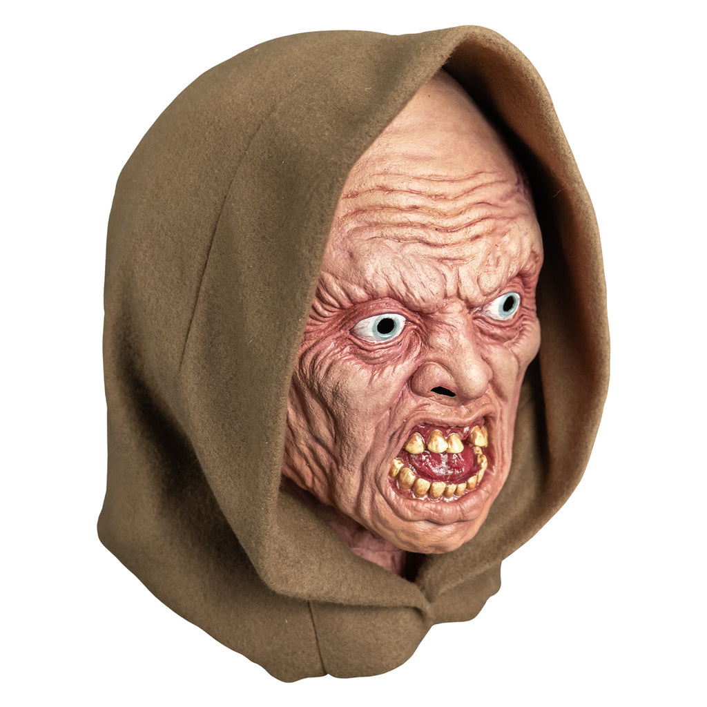 mask, right view. wearing tan hood. pink highly wrinkled flesh. no eyebrows, pale blue irises, mouth open in a snarl showing crooked yellowed teeth an shiny wet looking red tongue.
