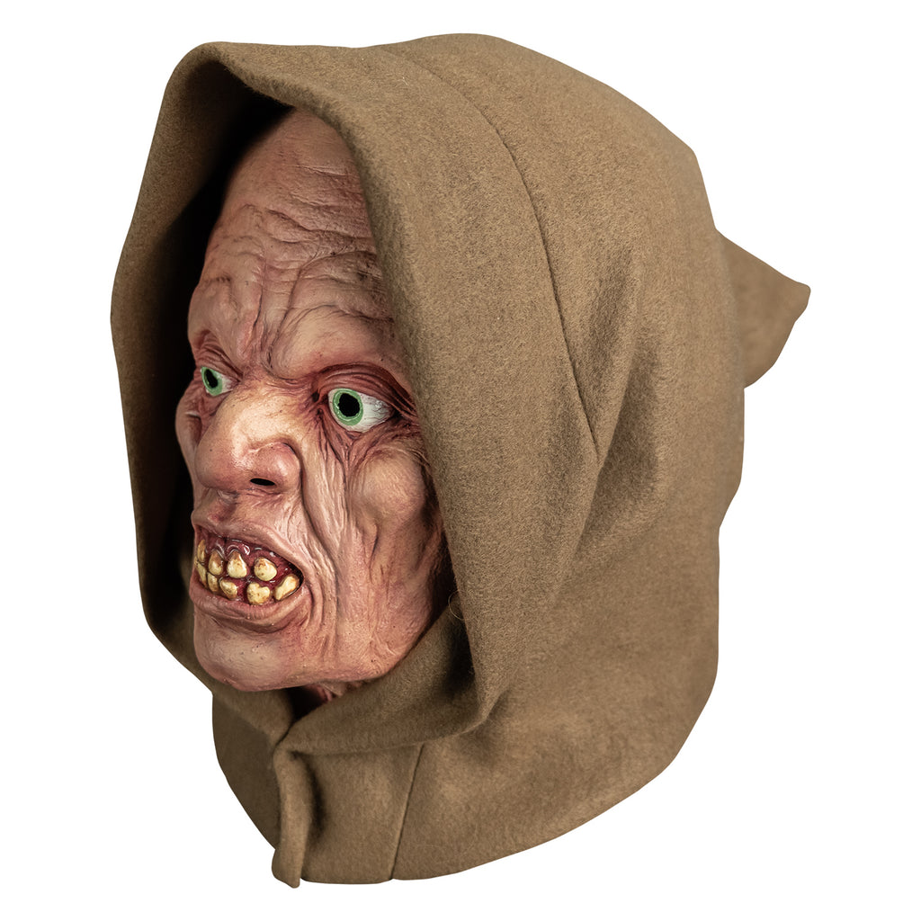 mask, left view. wearing tan hood. pink wrinkled flesh. no eyebrows, pale blue irises, lips open showing crooked yellowed teeth.