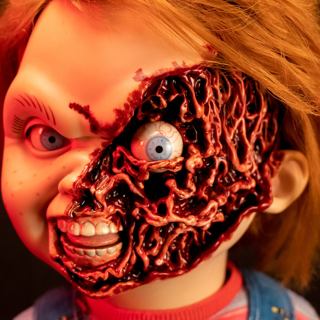 Dramatic red lighting. Ultimate Chucky Pizza Face additional head, slight left view. Red hair, blue eyes, freckles. Gory, fleshy left side of face, exposed eyeball. Mouth open, showing teeth and tongue.