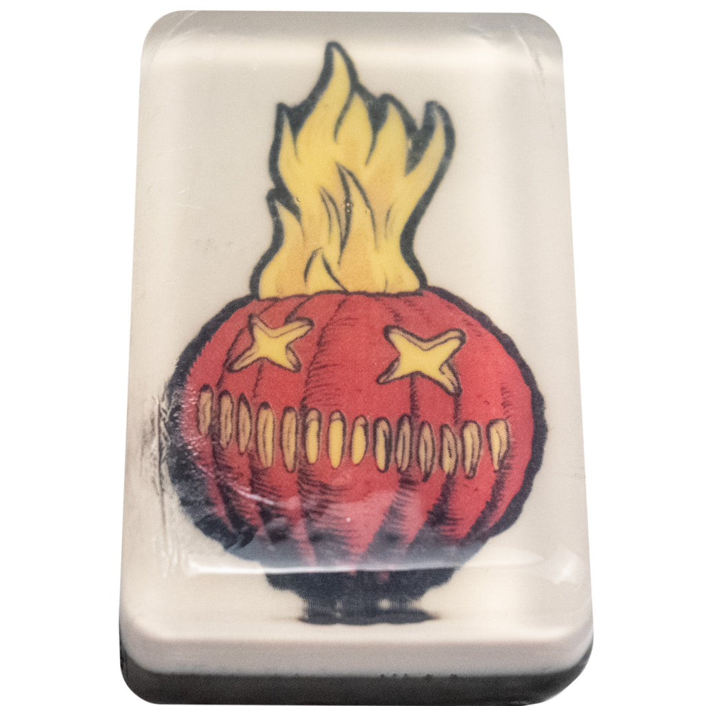 Bar soap. White, with illustration of Trick 'r Treat Sam-o-lantern under clear soap layer. Orange jack o' lantern face, two X eyes, several vertical hashmarks for a mouth, flames rising out of the top.