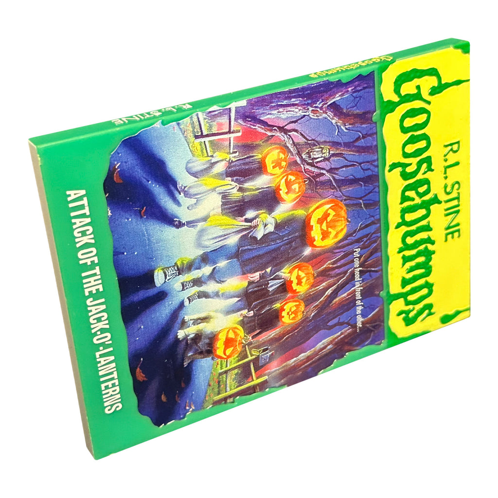 Magnet. Has the appearance of a book cover. Illustration of trick or treaters with jack o' lantern heads, walking on road, fences on both sides, trees in the background. Yellow banner at top, green text reads R.L. Stine, Goosebumps. White text on illustration reads Put one head in front of the other. Green border at bottom, white text reads Attack of the Jack 'o lanterns.