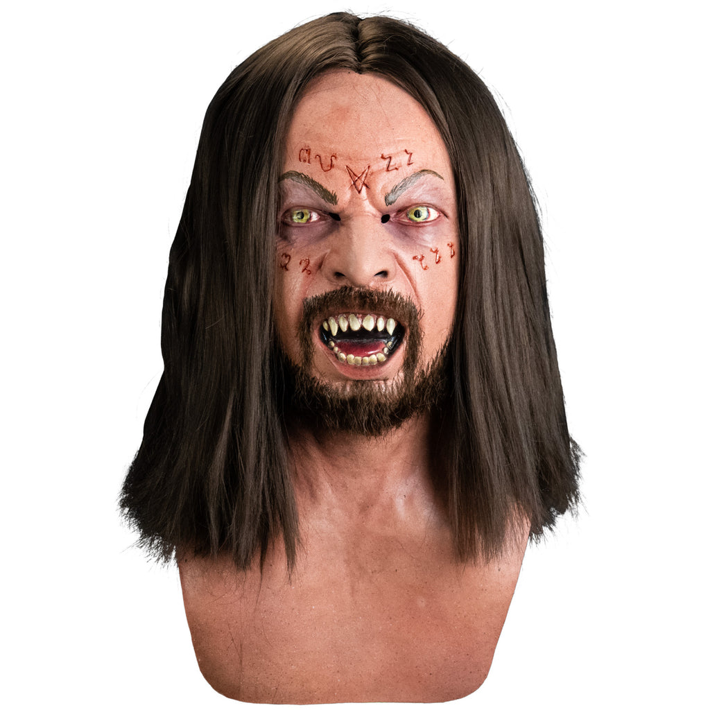 Mask, front view, head, neck and upper chest. Long, dark brown hair, brown eyebrows, green eyes, mouth open showing sharp teeth and red tongue, moustache and beard.  Occult symbols cut into forehead and upper cheeks.