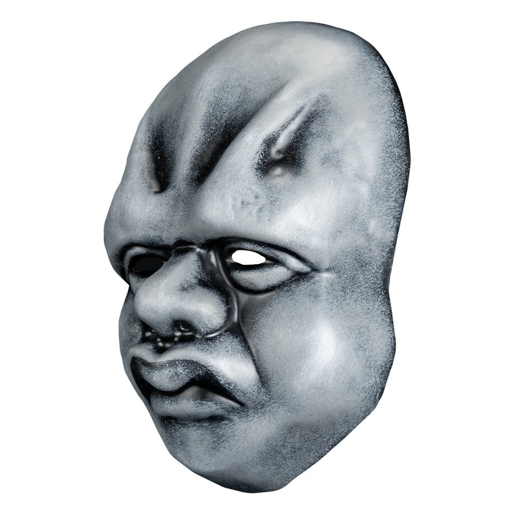 Mask, left view. Black and white toned face mask. Bald, ridges on forehead, no eyebrows, bags under small eyes, short fat nose, heavy cheeks and jowls, mouth with prominent frowning lips.