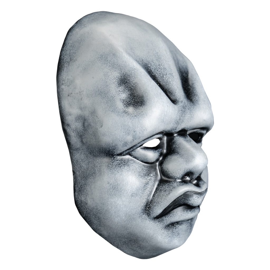Mask, right view. Black and white toned face mask. Bald, ridges on forehead, no eyebrows, bags under small eyes, short fat nose, heavy cheeks and jowls, mouth with prominent frowning lips.