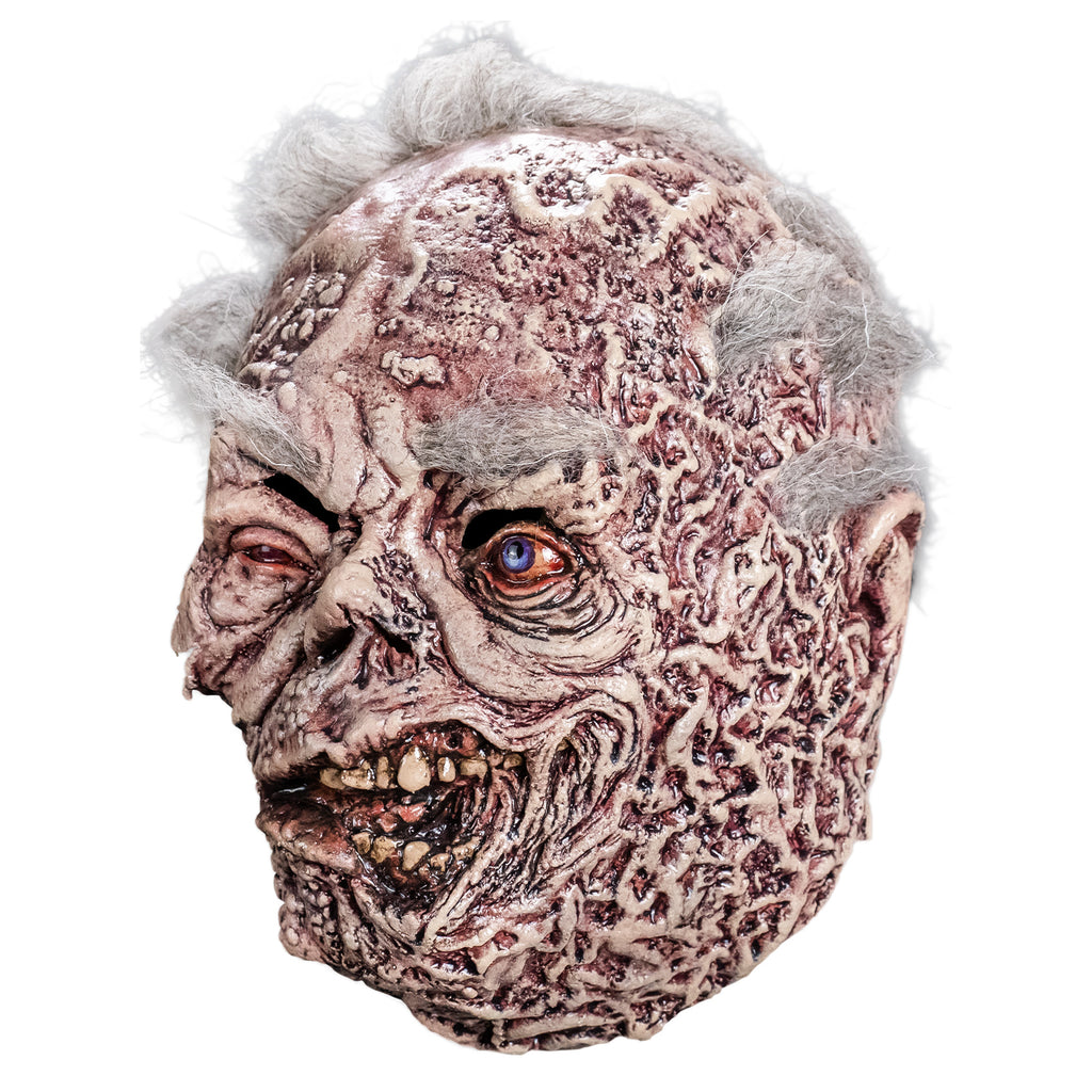 Mask, left side view. sparse short white hair, bushy white eyebrows. Mottled, wrinkled and sagging white and brown skin. Right eye squinting almost shut and watery. Bloodshot, open blue left eye. small deformed nose. Crooked rotting mouth, sagging bottom lip, slightly open showing some crooked and dirty teeth