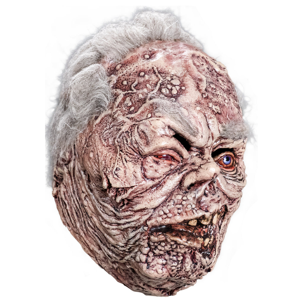 Mask, right side view. sparse short white hair, bushy white eyebrows. Mottled, wrinkled and sagging white and brown skin. Right eye squinting almost shut and watery. Bloodshot, open blue left eye. small deformed nose. Crooked rotting mouth, sagging bottom lip, slightly open showing some crooked and dirty teeth