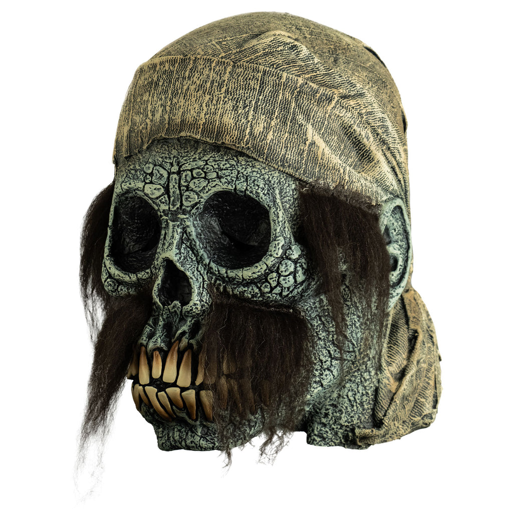 mask, left view. dirty off-white scarf on head hanging down to neck. Empty eye sockets, long brown sideburns and mustache. Cracked gray skull face with ears, long yellow teeth.