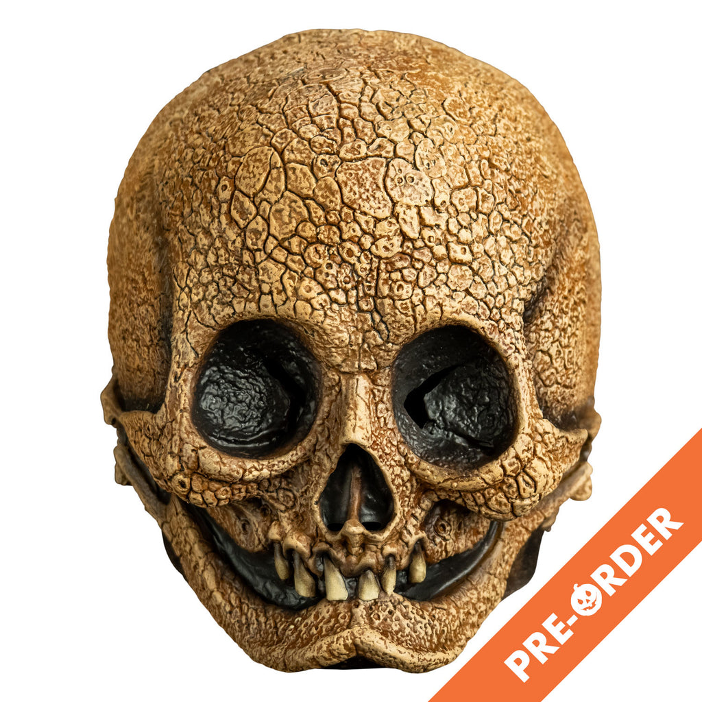 white background, orange diagonal banner at lowered right, white text reads pre-order.  Mask, front view. Tan, cracked textured Skull, empty eye sockets, 6 upper teeth in mouth, toothless lower jaw.