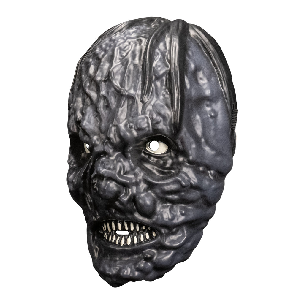 plastic mask. left side view. Black mottled and lumpy skin indistinct facial features. lips open showing small sharp white teeth.