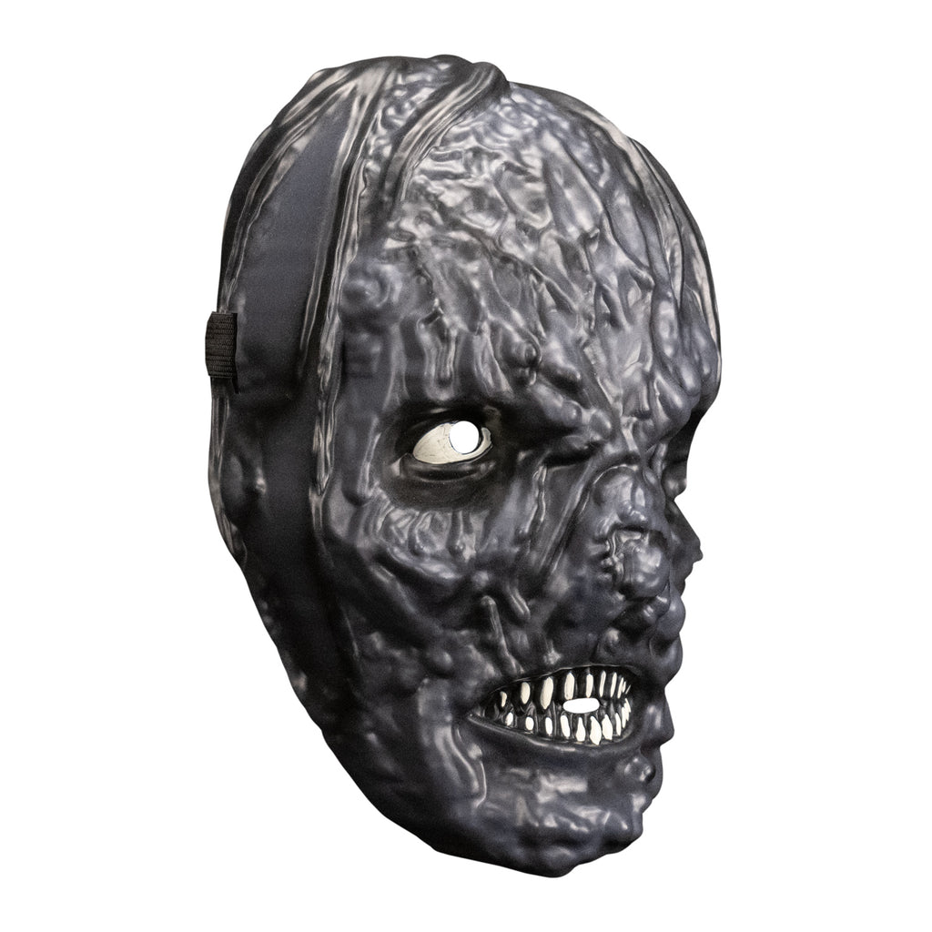 plastic mask. right side view. Black mottled and lumpy skin indistinct facial features. lips open showing small sharp white teeth.