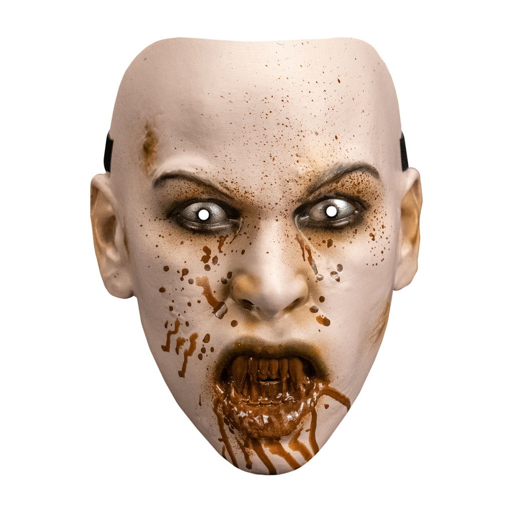 Plastic mask.  Front view. pale skin, blood spattered face.  brown arched eyebrows, black-rimmed white eyes. mouth with lips open showing sharp bloodstained teeth, blood dripping down chin.