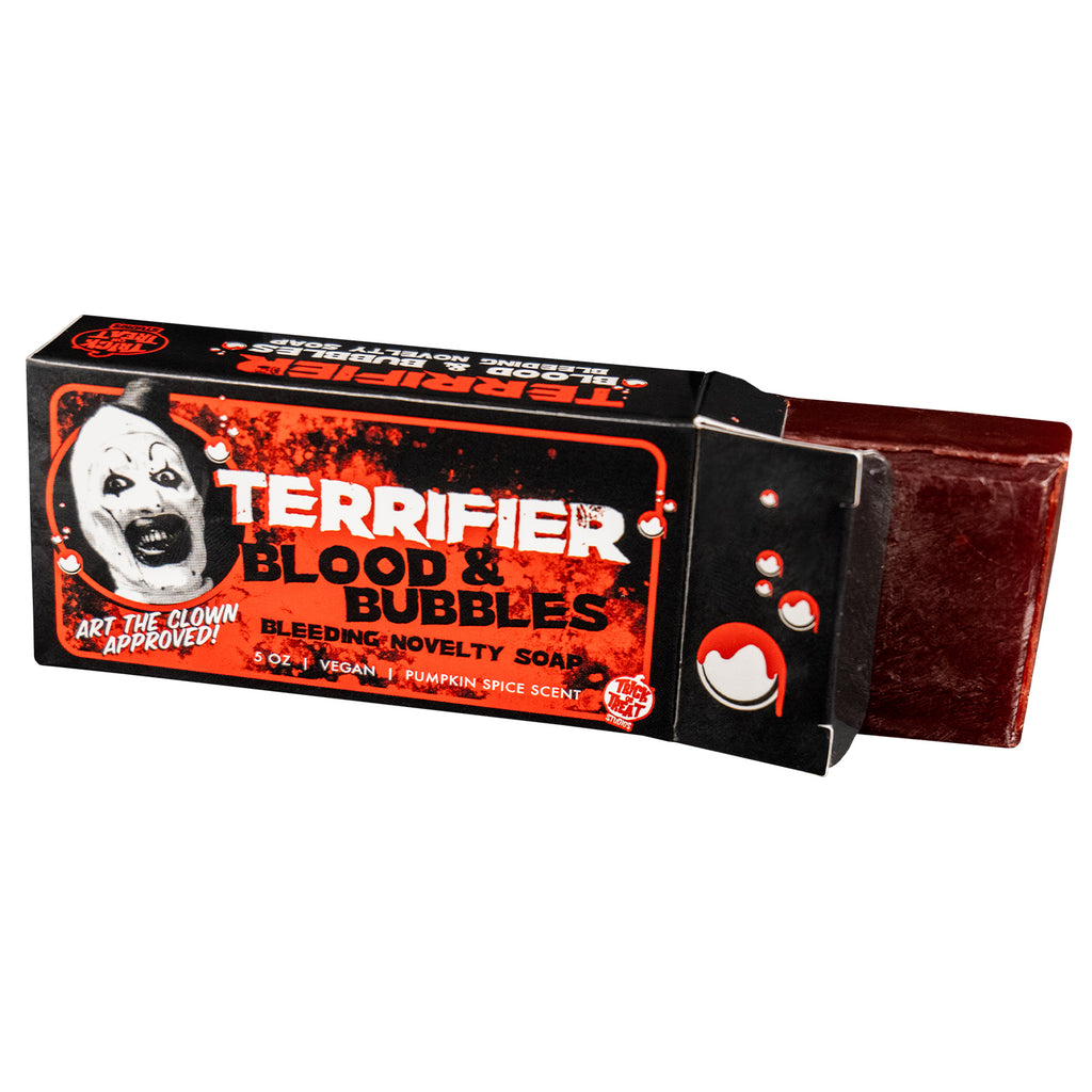 Terrifier soap in open packaging. Dark red soap bar coming out of black red and white box. Illustrated white bubbles with dripping red blood. Black and white illustration of Art the clown head. White text reads Terrifier, Art the clown approved, 5 ounce, vegan, pumpkin spice scent. Black text reads Blood & Bubbles, Bleeding novelty soap. Red and white Trick or Treat Studios logo bottom right.