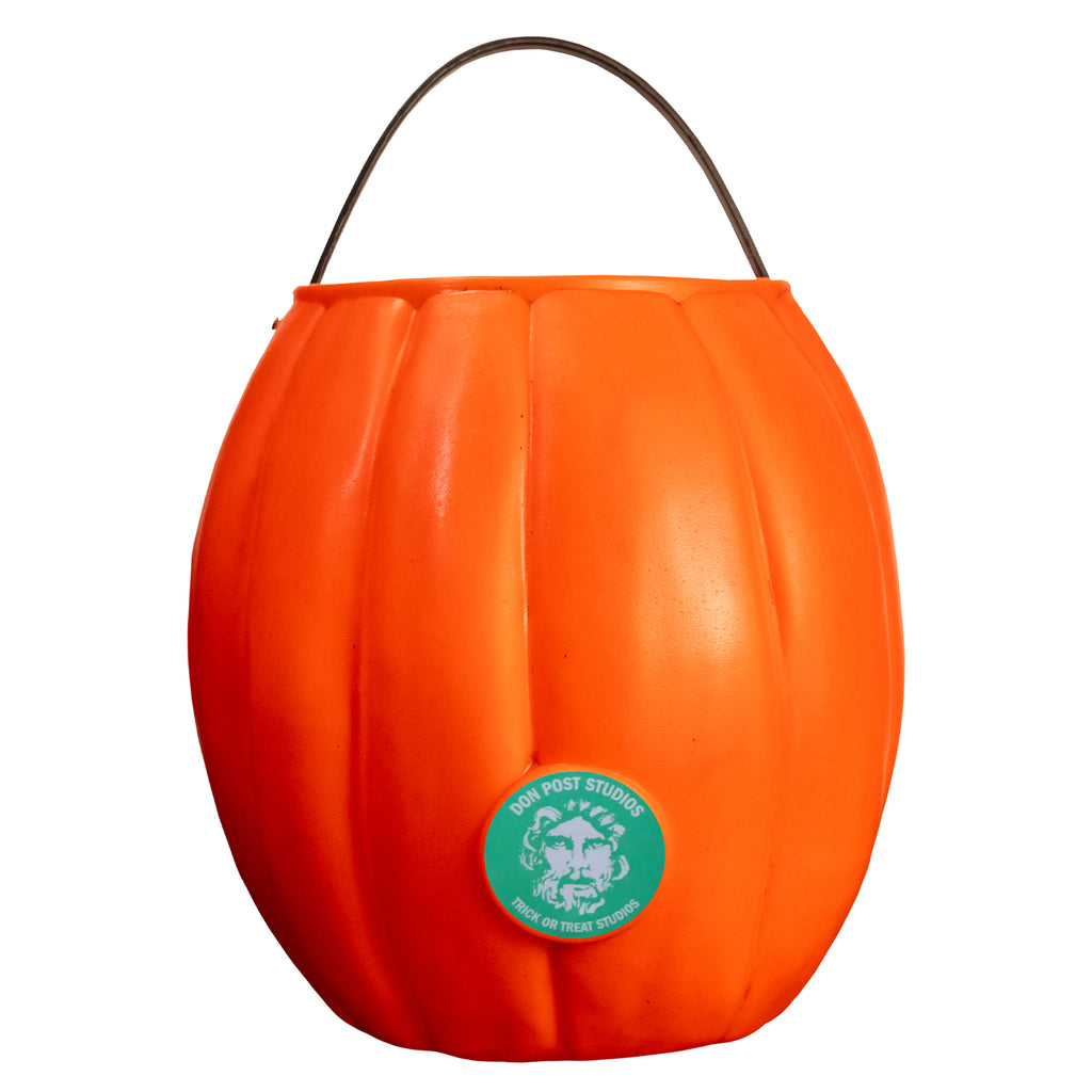 Back view pumpkin candy pail. Orange with Light green-blue circle near the bottom in the center, illustration of face, white text reads Don Post Studios, Trick or treat studios. Black handle at top. 
