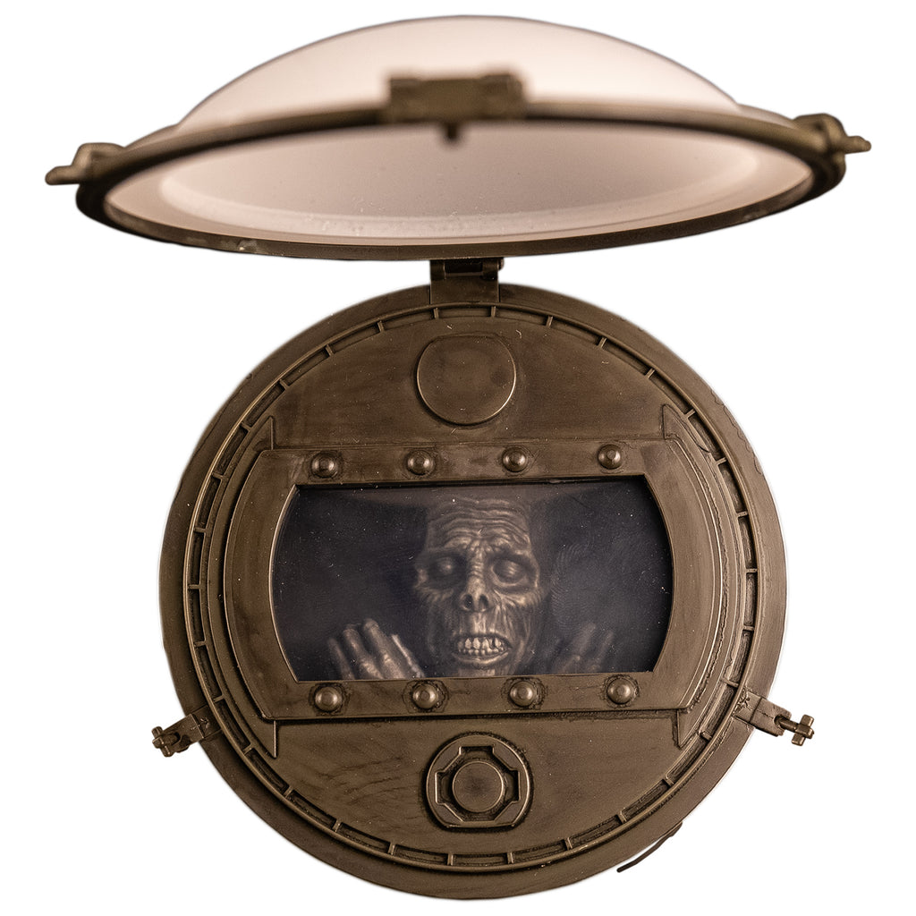 Closeup overhead view of top of barrel. showing white lid, latches and window under lid, corpse face, eyes closed, and hands shown under window
