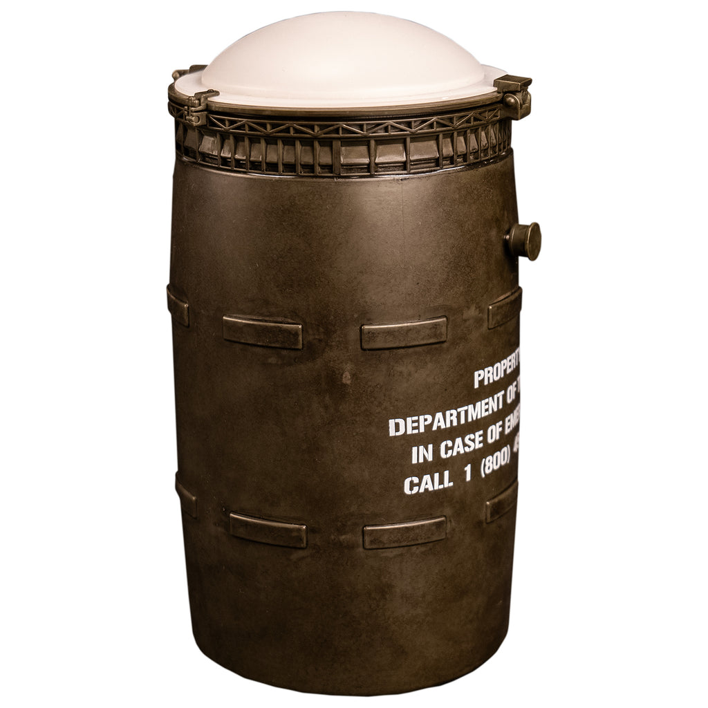 side view Black barrel with white lid, white text reads property of the army in case of emergency call 1 800 454-8000. 