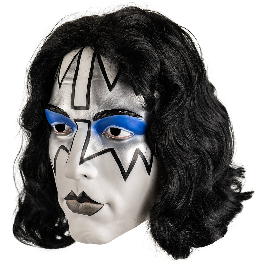 Kiss Spaceman plastic mask left view. Long black hair, white face, Black eyebrows, blue eyeshadow on eyelids, surrounded with silver painted angular shapes outlined in black from the edges of the forehead to the cheekbones, black and gray painted lips.