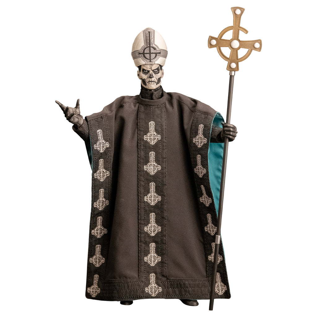 White background. Figure and accessories. Black and white skull-like face wearing black and silver, tall hat adorned with black inverted cross with semi circle that looks like a G. wearing black floor-length robe green on the inside adorned with several white inverted crosses, with semi circle that looks like a G. black gloves and black boots. Holding black staff topped with inverted gold cross.
