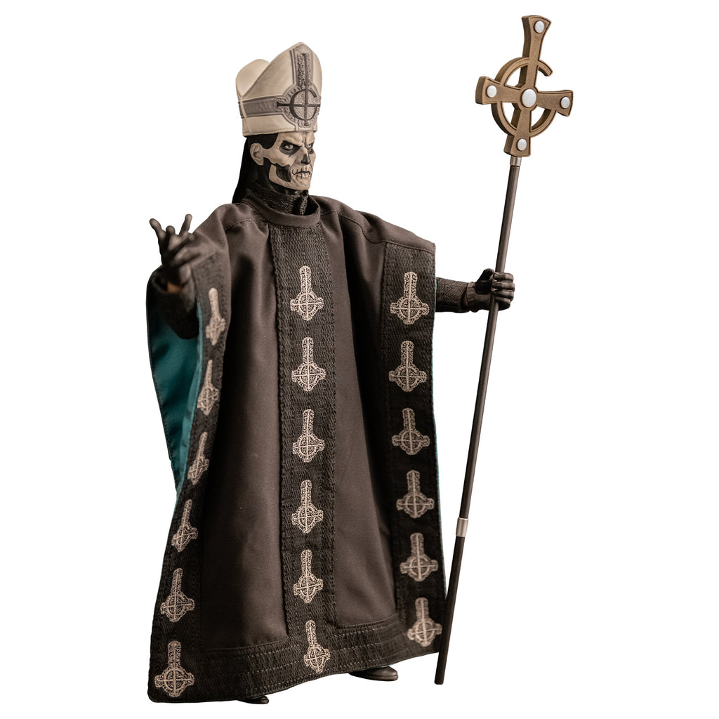 Right side view. White background. Figure and accessories. Black and white skull-like face wearing black and silver, tall hat adorned with black inverted cross with semi circle that looks like a G. wearing black floor-length robe green on the inside adorned with several white inverted crosses, with semi circle that looks like a G. black gloves and black boots. Holding black staff topped with inverted gold cross.