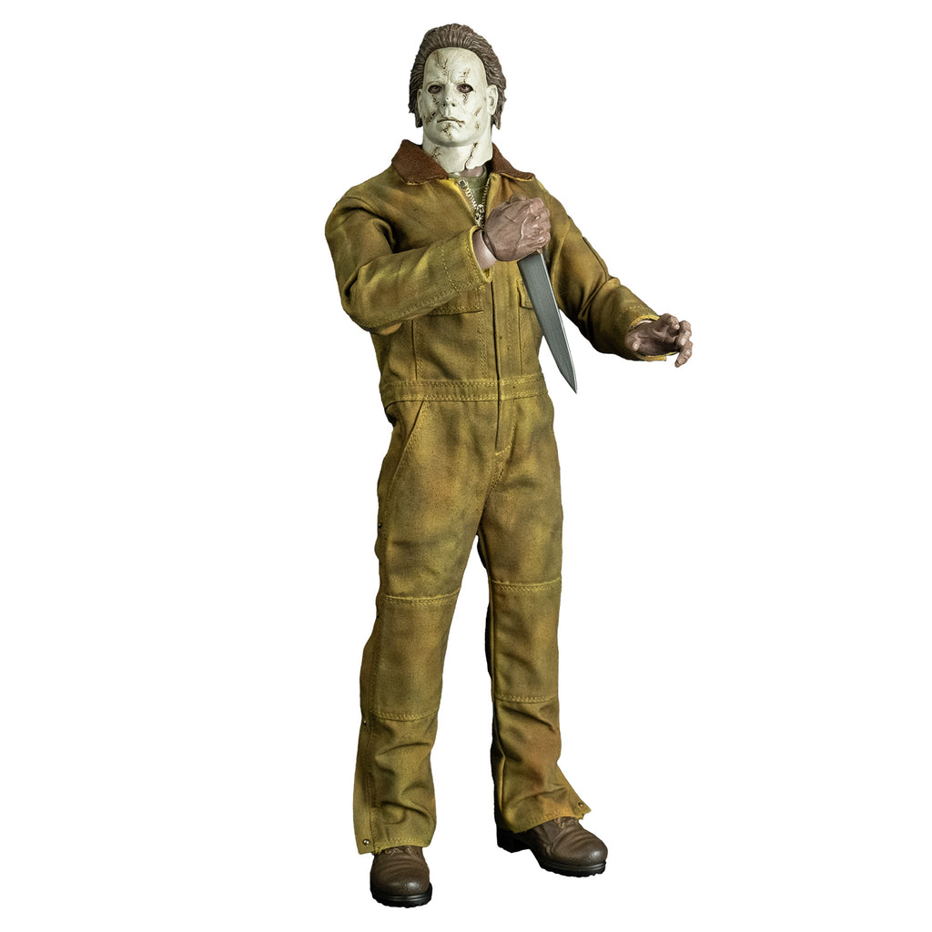 Front view, Michael Myers 1:6 scale action figure. Wearing Halloween 2007 mask head turned to the right, tan coveralls, brown boots. holding kitchen knife in  right hand raised to the chest, left hand in grabbing position raised above waist.