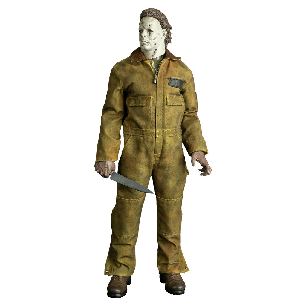 Front view, Michael Myers 1:6 scale action figure. Wearing Halloween 2007 mask head turned to the right, tan coveralls, brown boots. holding kitchen knife in right hand at his side, left hand in grabbing position at side.