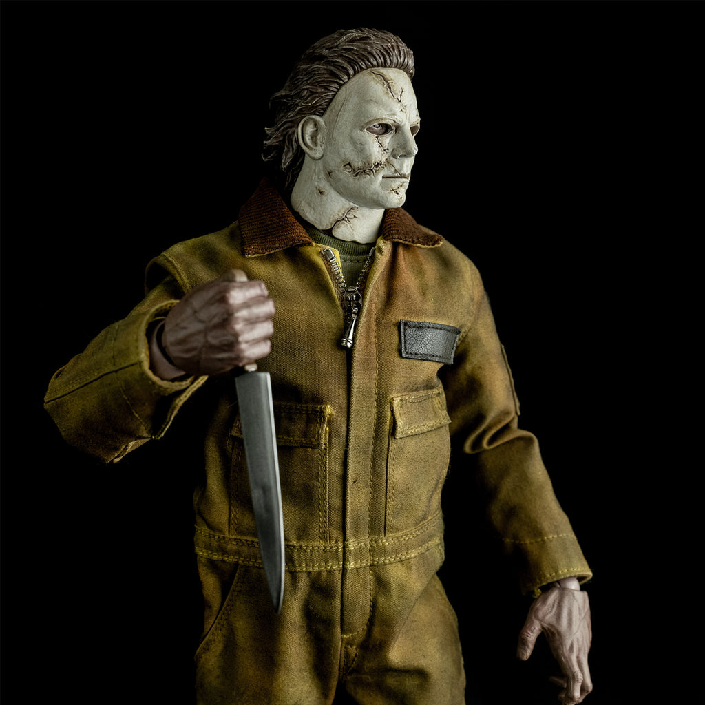 close up, slight right view, above hips. Dramatic lighting. Michael Myers 1:6 scale action figure. Wearing Halloween 2007 mask, tan coveralls. holding kitchen knife in right hand raised to the chest, left hand in grabbing position at waist.