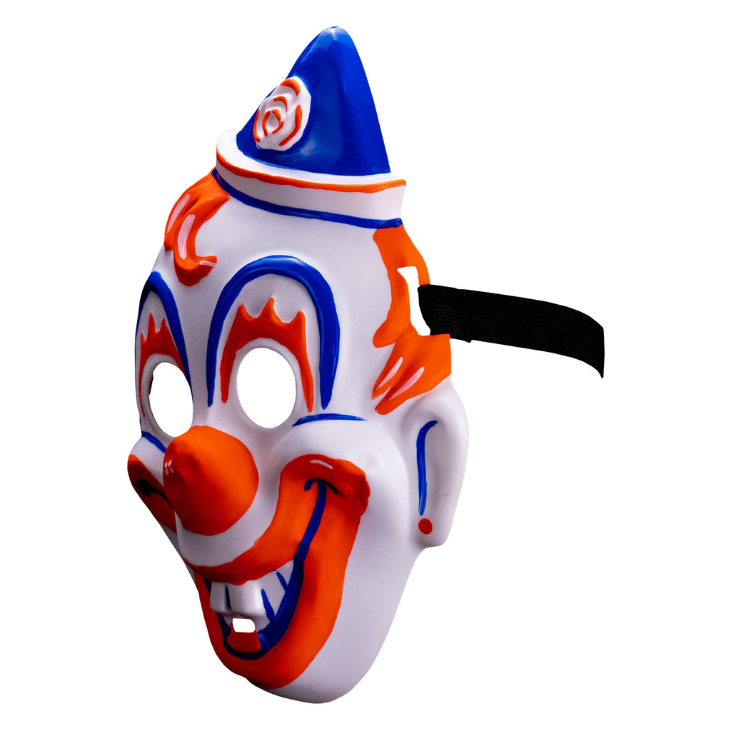 Face mask, left side view. white clown face, blue white and orang triangular hat tipped to the left . orange painted hair. Blue arches around eyes, orange painted eyelashes, blue lines on cheeks and ears, orange dots on earlobes, large orange clown nose. Orange and blue clown mouth in a large smile showing teeth. Black elastic strap at temples