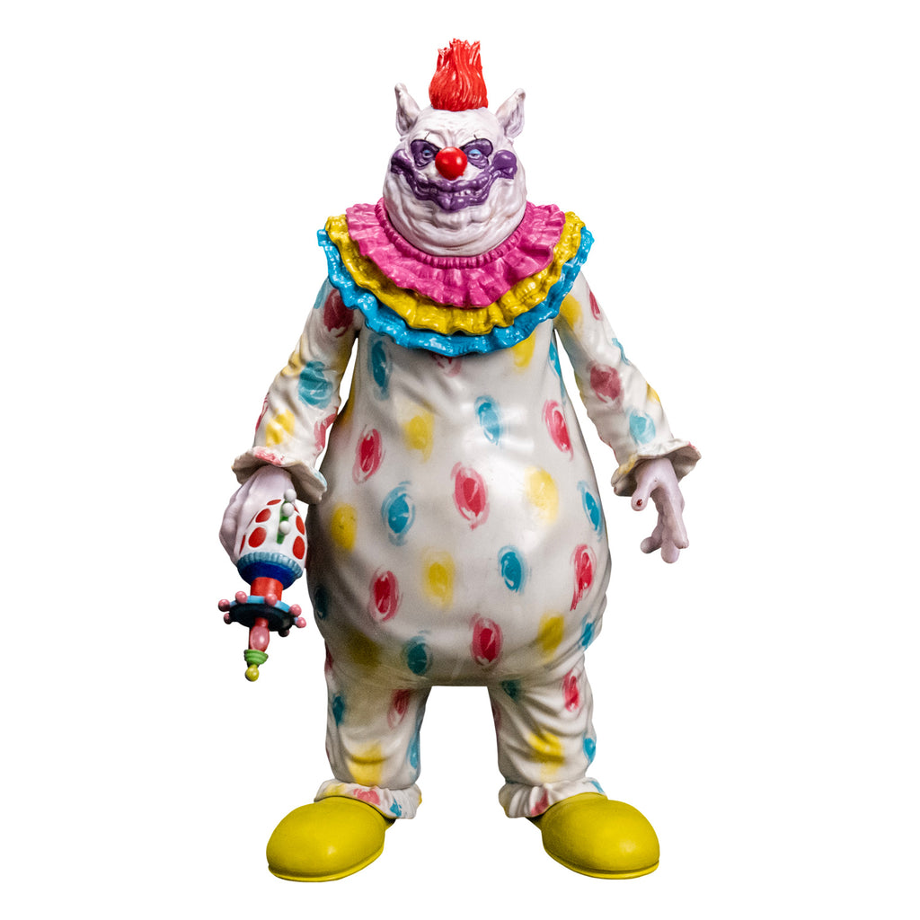 Figure, front view.  Lumpy and wrinkly face with several flesh folds beneath chin, large pointed ears on side of head. White skin, red hair on top, purple around eyes, large dark pink nose and lumpy purple clown mouth.  wearing white clown suit with pink, blue and yellow circles on it.  Pink, yellow and blue ruffles at neck,  ruffled at wrists and ankles.  White hands, right hand holding ray gun.  Large yellow shoes.