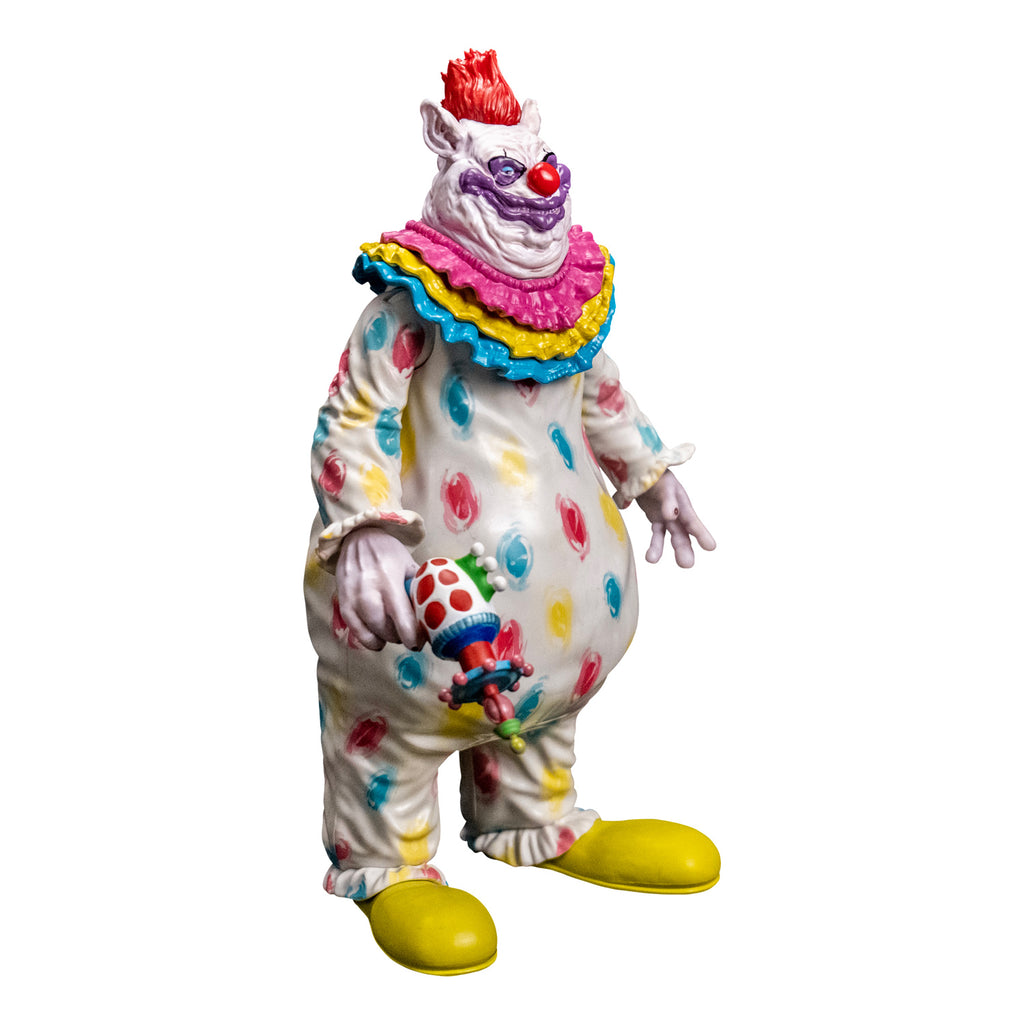 Figure, right side view. Lumpy and wrinkly face with several flesh folds beneath chin, large pointed ears on side of head. White skin, red hair on top, purple around eyes, large dark pink nose and lumpy purple clown mouth. wearing white clown suit with pink, blue and yellow circles on it. Pink, yellow and blue ruffles at neck, ruffled at wrists and ankles. White hands, right hand holding ray gun. Large yellow shoes.