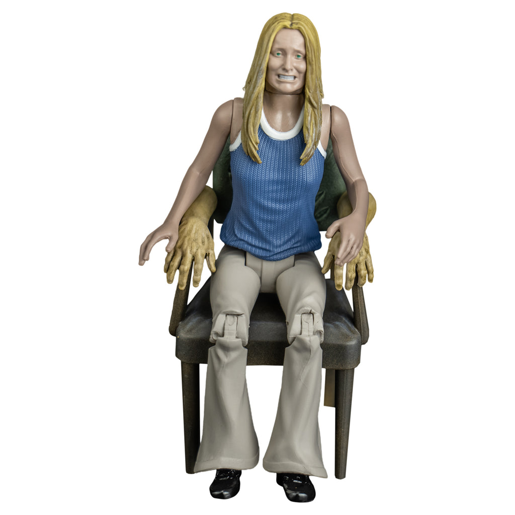 Sally figure, front view.  Blond woman, grimace on face, blue and white tank top, tan flare legged pants.  Sitting in chair with human arms.