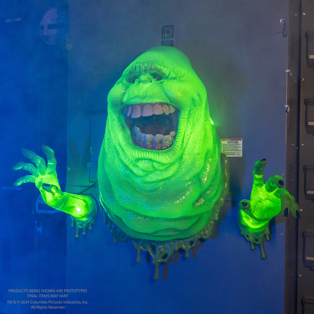 Wall mounted ghost.  Bright green lighted ghost, lumpy blob with small eyes and nose, large open mouth showing large square teeth and tongue.  hands separately mounted on wall lighted bright green with dark fingernails.  slime dripping around edges at the wall.