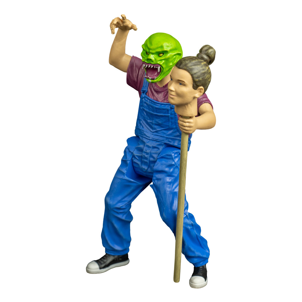 goosebumps figure, left view.  Wearing haunted mask,Bright green skin, no hair. Angry face with large ears, yellow eyes, large snarling mouth with sharp white teeth, pink tongue and gums. white drool on lower jaw and chin. Purple t-shirt, blue overalls, black and white sneakers.  Right arm bent at elbow raised over head.  left hand holding staff with person's head attached, brown hair pulled back in a bun.