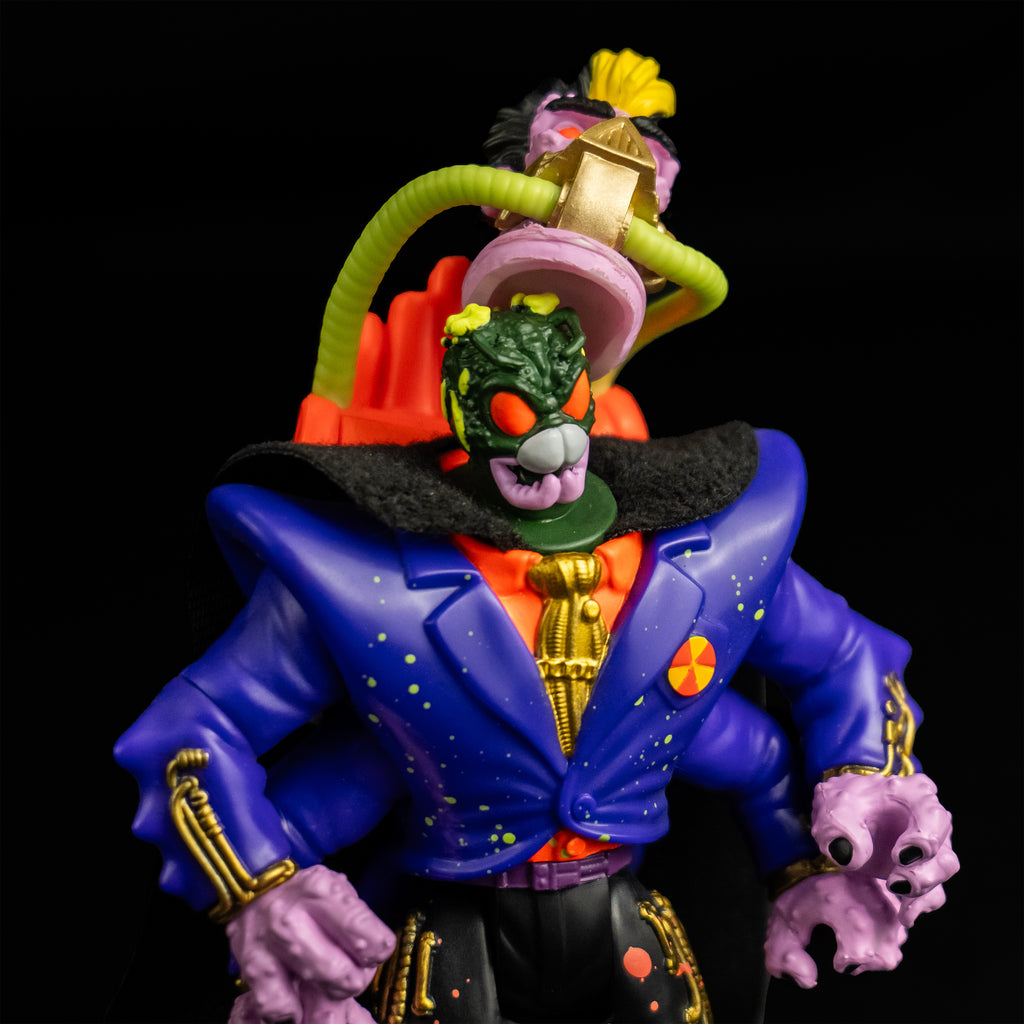 Black background. Action figure, front view closeup. Humanoid head removed atttached by hoses to an orange backpack. Green bug head revealed green and yellow flesh, large orange eyes, white and pink mandibles. Wearing orange shirt with a gold tie, blue jacket, black cape, four arms, black pants with orange splatter.