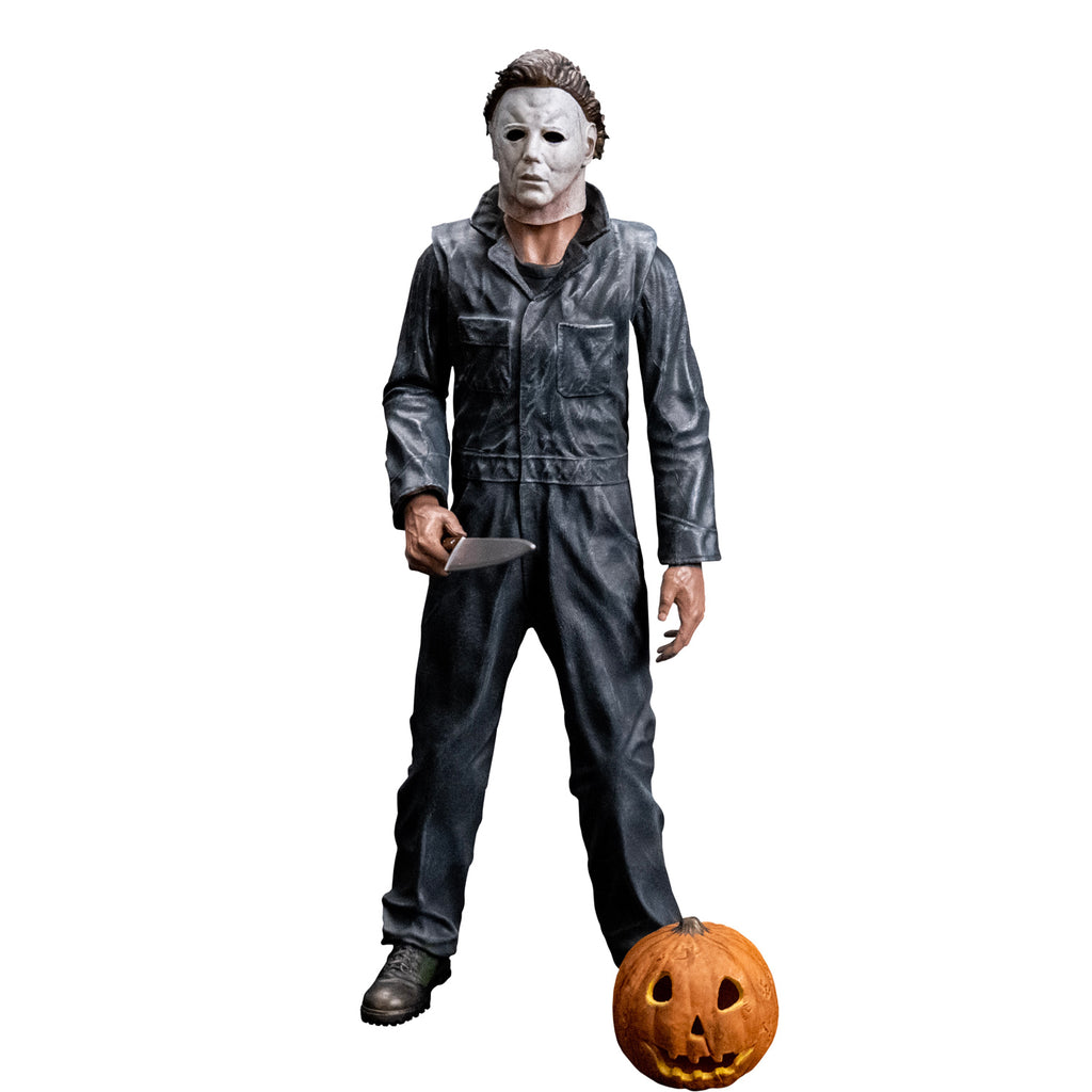 Front view, Michael Myers 8 inch action figure. Wearing Halloween (1978) Michael Myers mask, dark coveralls, black boots. holding a kitchen knife in right hand. Orange jack o' lantern resting on ground in front of the figure