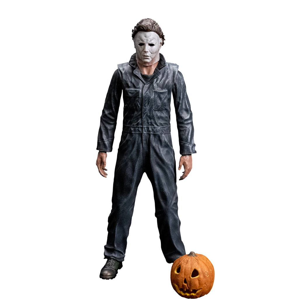 Front view, Michael Myers 8 inch action figure. Wearing Halloween (1978) Michael Myers mask, dark coveralls, black boots. arms at sides. Orange jack o' lantern resting on ground in front of the figure