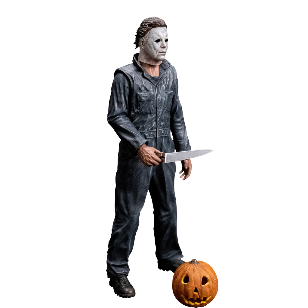 Slight right view, Michael Myers 8 inch action figure. Wearing Halloween (1978) Michael Myers mask, dark coveralls, black boots. holding a kitchen knife in right hand. Orange jack o' lantern resting on ground in front of the figure