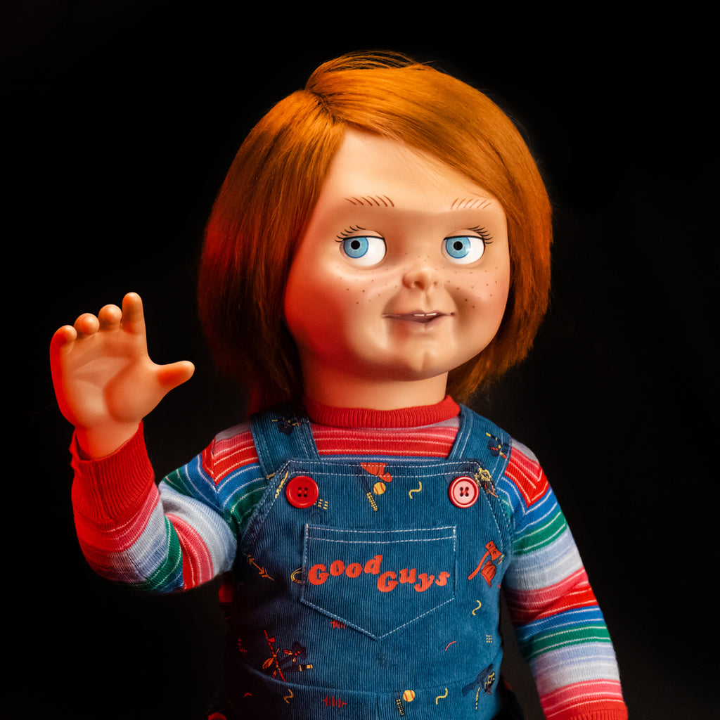 Dramatic red lighting. Close up of Ultimate Chucky doll additional head, Good Guy Tommy, attached to doll wearing striped shirt under blue overalls. Red hair, blue eyes, freckles, accessory open right hand raised.