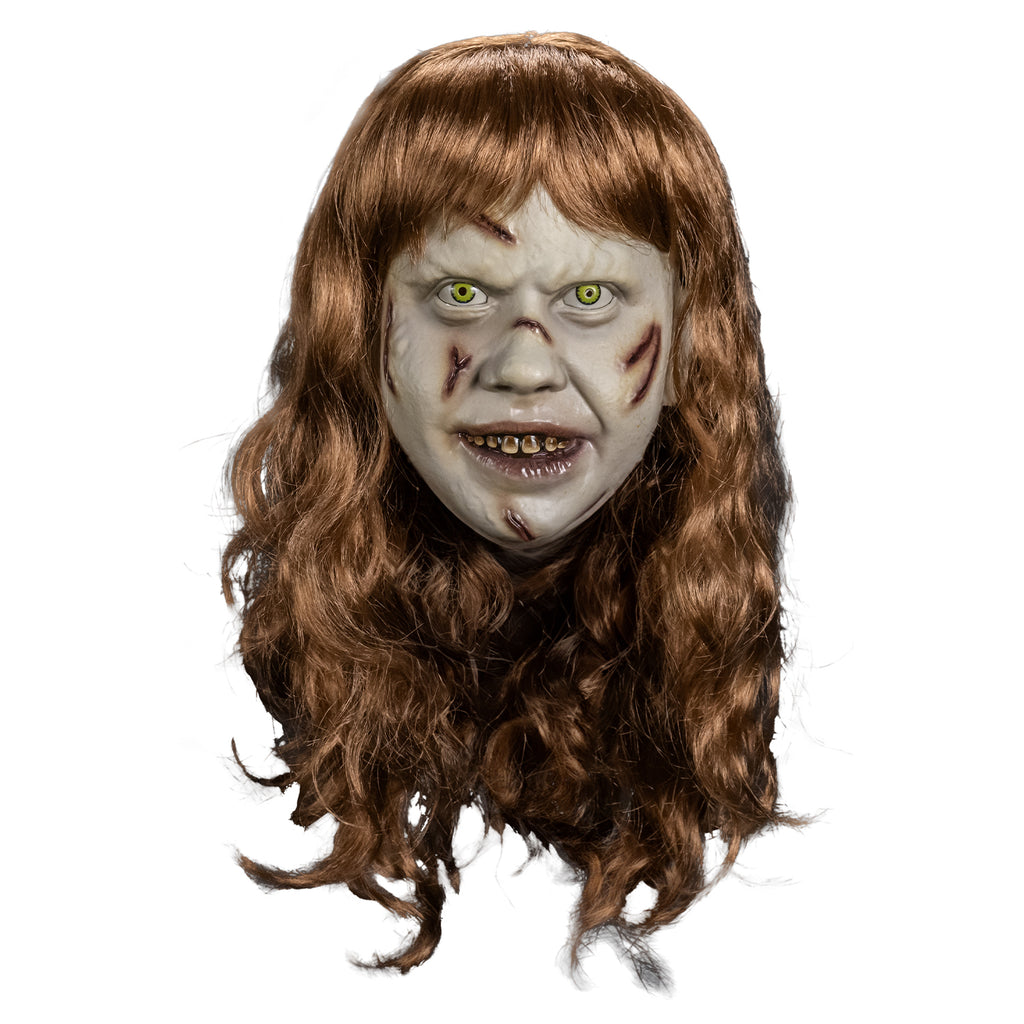 Plastic face mask front view.  Girl's head, long, pale skin, light brown, wavy hair with bangs.  Furrowed brow, no eyebrows, yelllow-green irises and small pupils in the eyes. red-brown wounds on right forehead, both cheeks, nose and chin.  Mouth slightly open, showing dirty brown upper teeth, shiny wet looking lips.