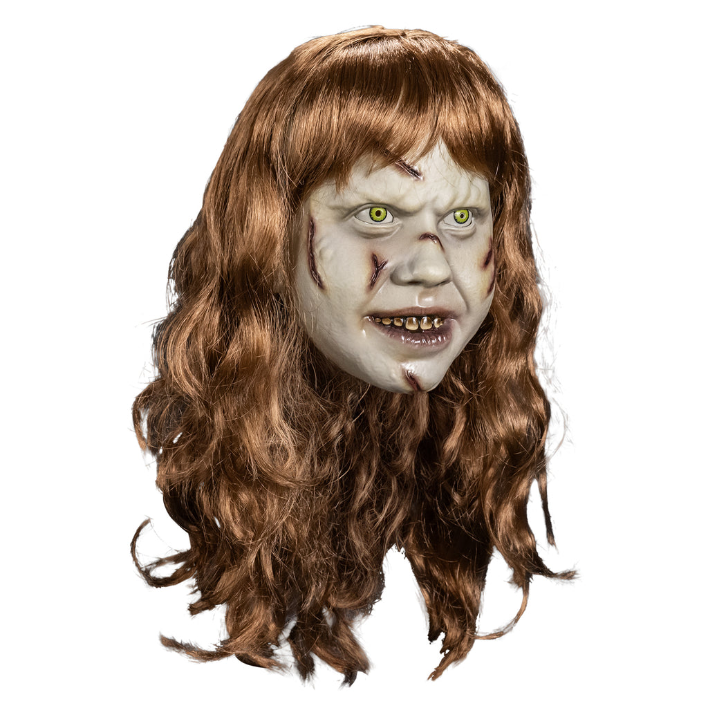 Plastic face mask right view. Girl's head, long, pale skin, light brown, wavy hair with bangs. Furrowed brow, no eyebrows, yelllow-green irises and small pupils in the eyes. red-brown wounds on right forehead, both cheeks, nose and chin. Mouth slightly open, showing dirty brown upper teeth, shiny wet looking lips.