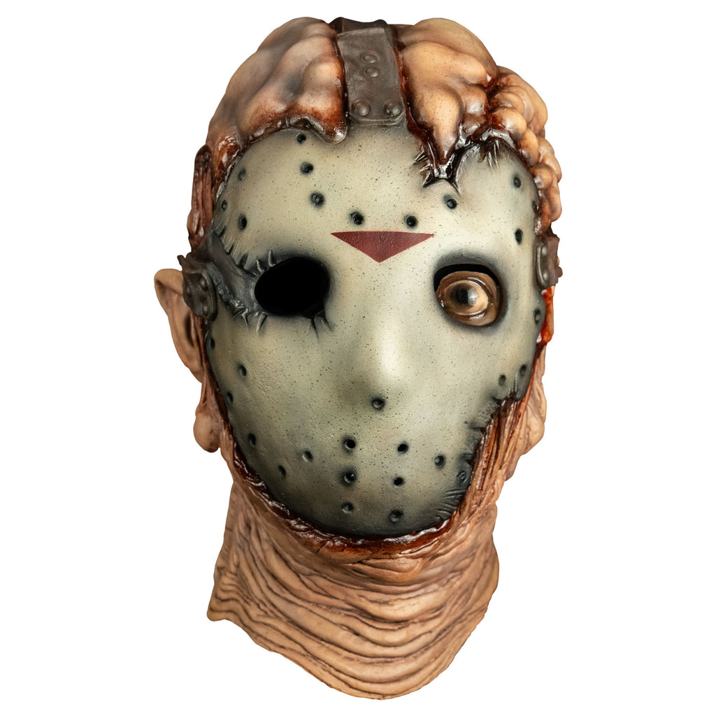 Mask, front view. lumpy and damaged flesh on top of head, tattered, dirty hockey mask on face, brown straps at top and sides of head from forehead and temples going back. Right empty eye socket, Brown, left eye open, wrinkled and sagging flesh around chin and neck.