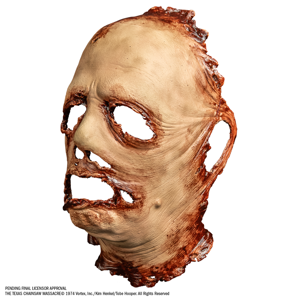 mask, left view. gory flesh, deformed facial features. has open space where left ear should be. Bloody around margins of face and neck, eye, nose and mouth holes