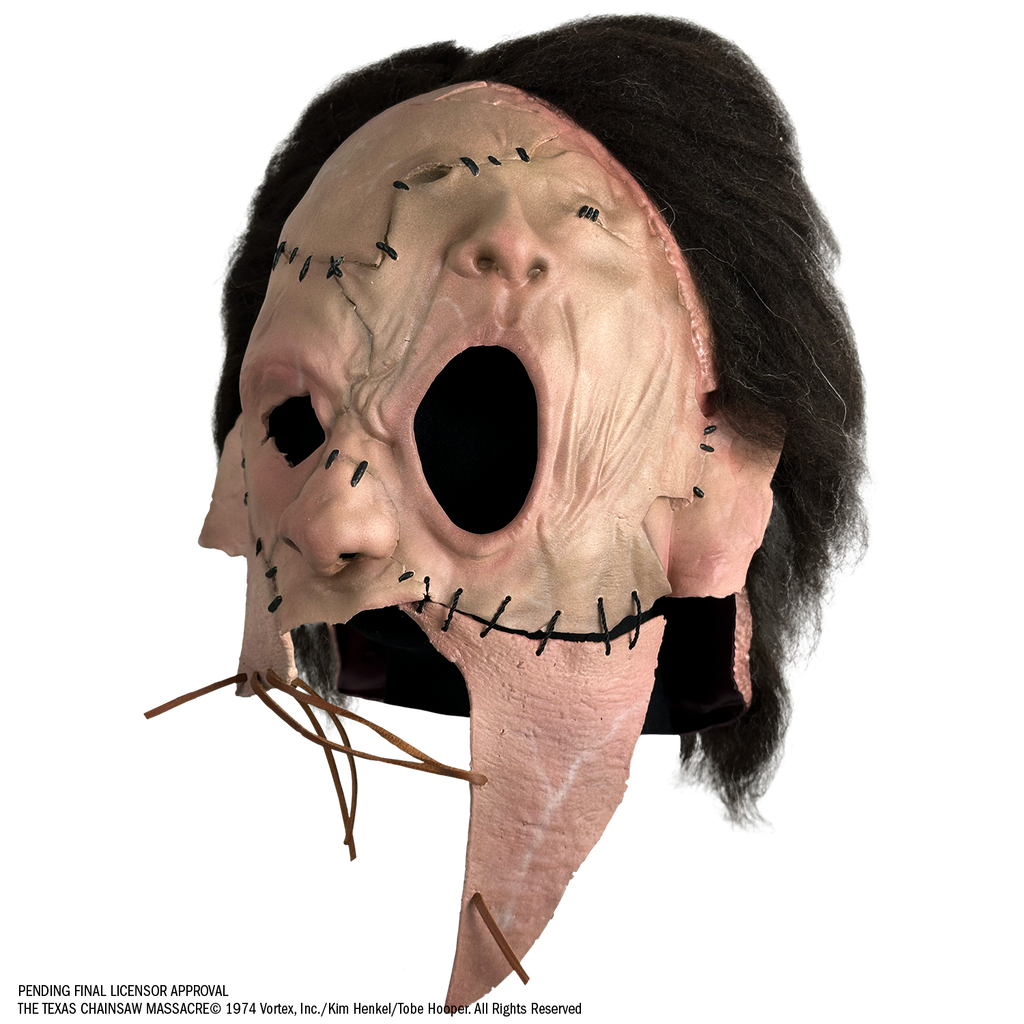 Mask, left view, short, dark brown, bushy hair, skin is sewn together, stitches around forehead, cheeks and ears, patch of skin over left eye and forehead is shaped like a nose and mouth. Lower face is open below nose with leather stitching across.