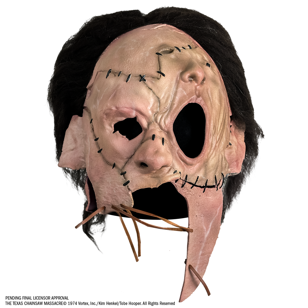 Mask, front view, short, dark brown, bushy hair, skin is sewn together, stitches around forehead, cheeks and ears, patch of skin over left eye and forehead is shaped like a nose and mouth. Lower face is open below nose with leather stitching across.