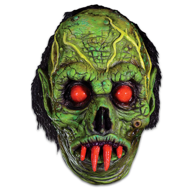 Mask, front view. Green wrinkled and decaying flesh, bulging yellow veins on forehead, black hair, black-rimmed red-orange eyes, four red orange fangs in mouth. Pointed ears.