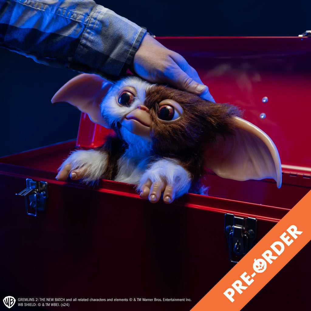 Glam shot. Gizmo mogwai prop, sitting in a red toolbox, man's hand patting his head, brown and white fur large brown eyes, large pointed tan ears. Hairless hands. White text at bottom is licensing information for the product. Orange diagonal banner at bottom right corner, white text reads pre-order.