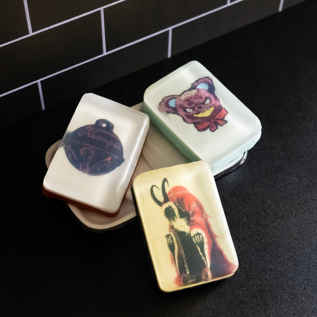 3 variations of soap, Krampus bell, Teddy Bear, and Krampus.  Set in soap dish on black counter.