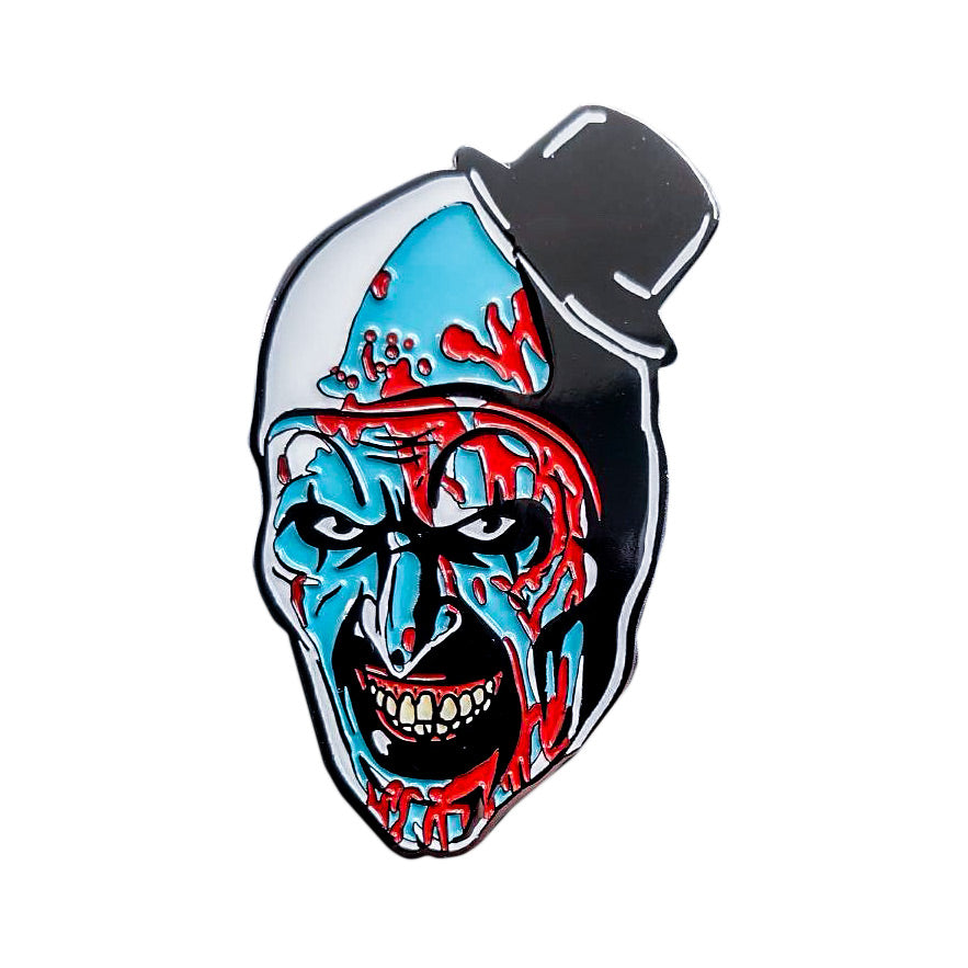 Enamel pin.Evil grinning, black and white clown face, blood spattered, blue shading, high black painted eyebrows, black around eyes and mouth, black dot on tip of nose, pink gums and crooked teeth. wearing a tiny black top hat.